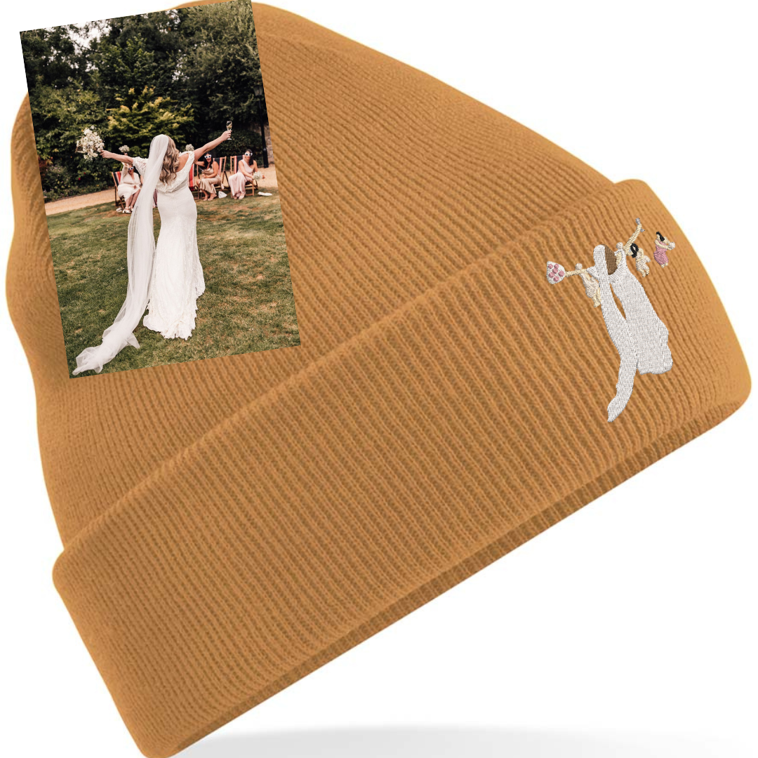 A caramel coloured beanie hat with a picture of someones wedding embroidered on to it.