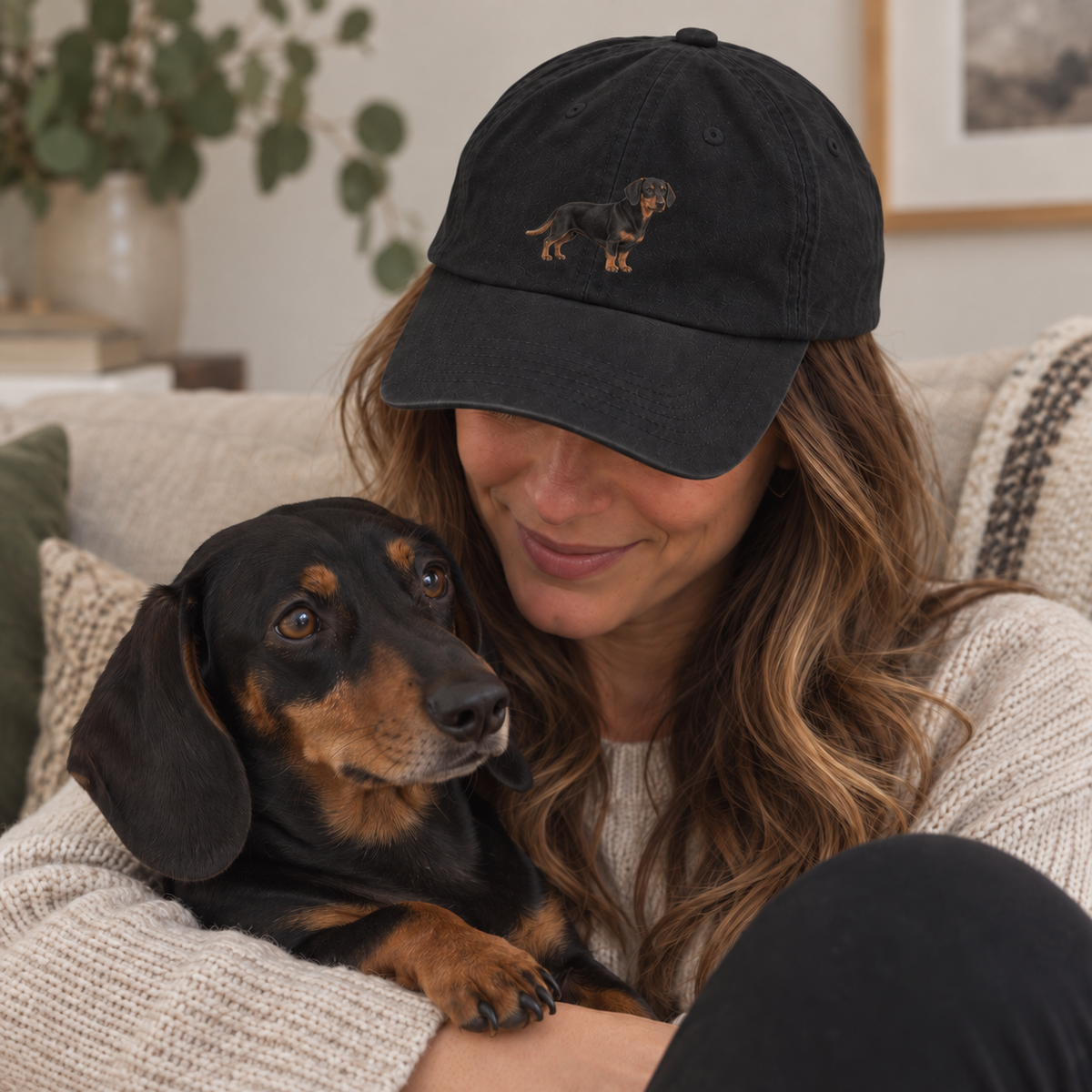 Woman wearing a custom embroidered brushed pet portrait cap with a full-body dachshund design in a cosy home lifestyle photo
