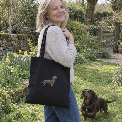 Woman carrying a black personalised embroidered dachshund portrait tote bag with her dog in a garden