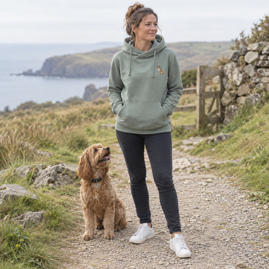Woman wearing a personalised embroidered pet portrait cross neck hoodie in dusty green with her dog on a coastal walk