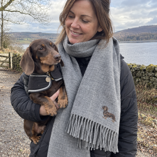 Woman wearing a personalised embroidered pet portrait scarf in heather grey with her dachshund in a natural outdoor UGC photo