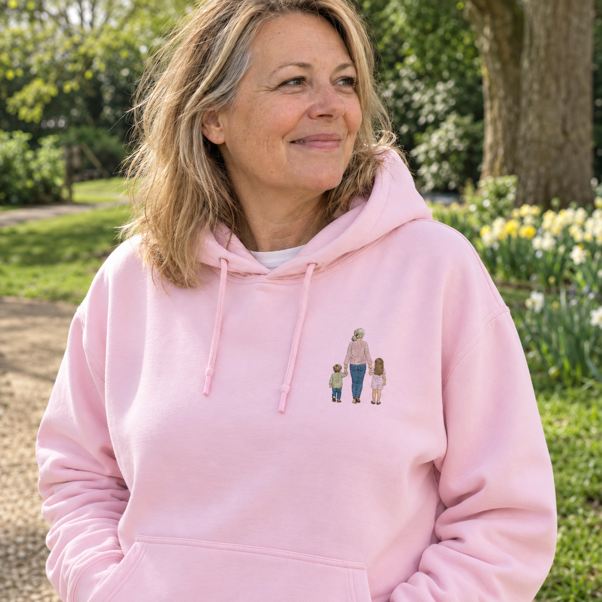 Woman wearing a Baby Pink personalised embroidered photo hoodie with a small full-colour grandparent and two children design in a natural park setting