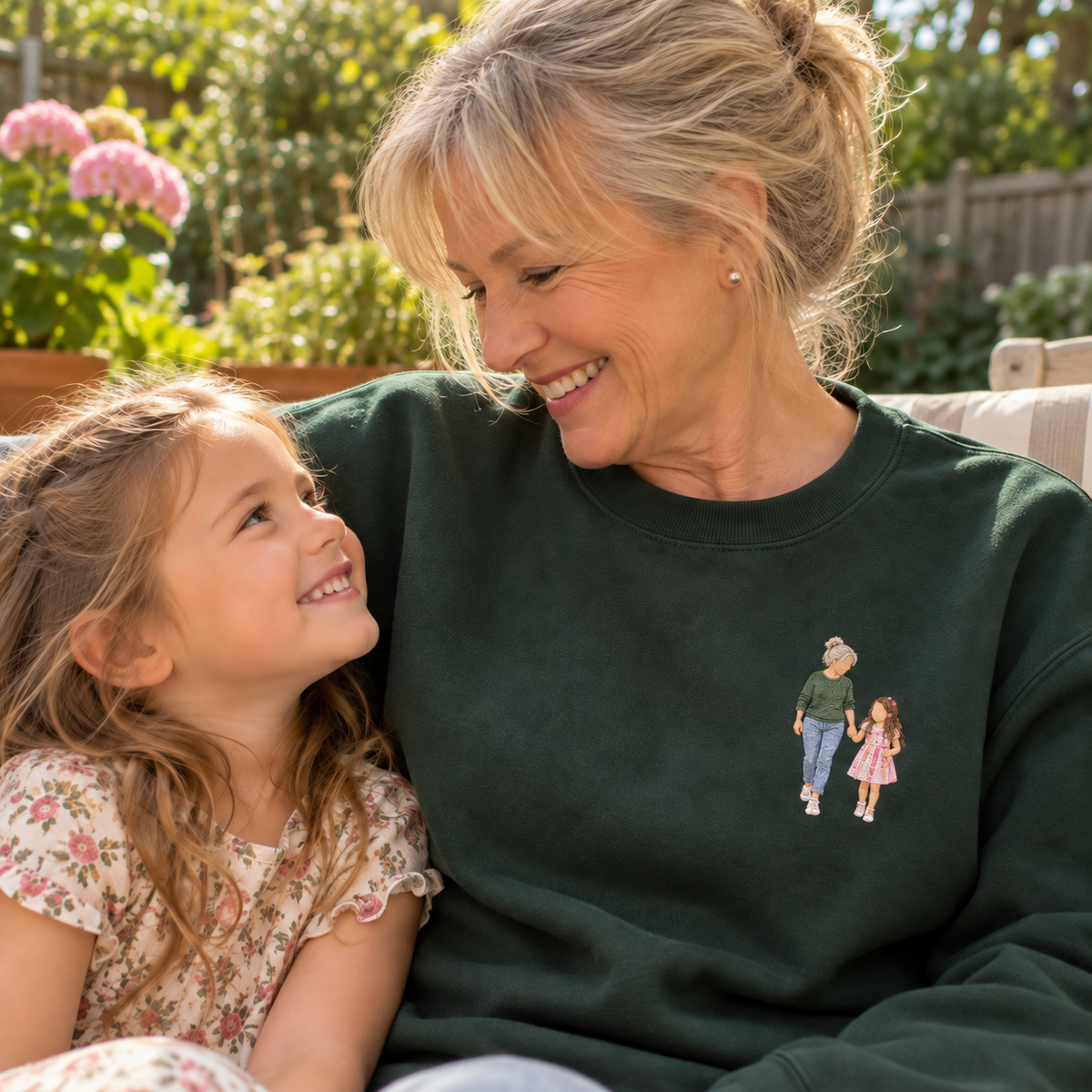 Grandmother wearing a personalised embroidered sweater with a full-colour faceless portrait of her and her granddaughter in a natural garden setting