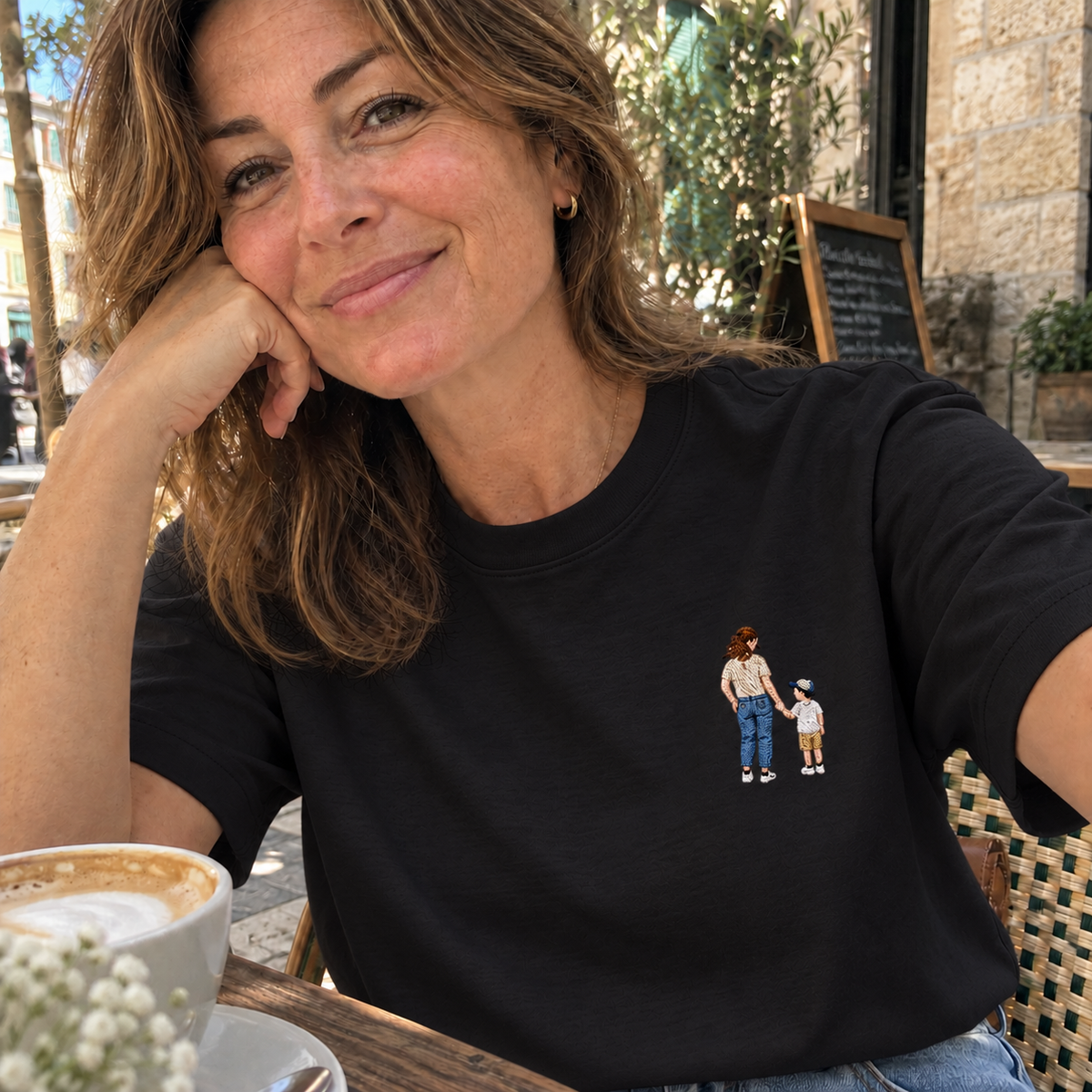 Woman wearing a black personalised embroidered T-shirt with a small full-colour mother and child portrait in a casual café setting