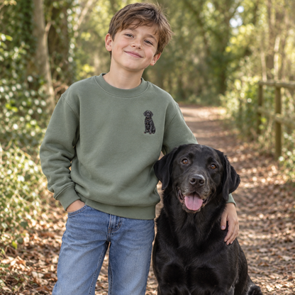 Boy wearing a personalised embroidered kids pet portrait sweater in green with a black Labrador on a woodland walk