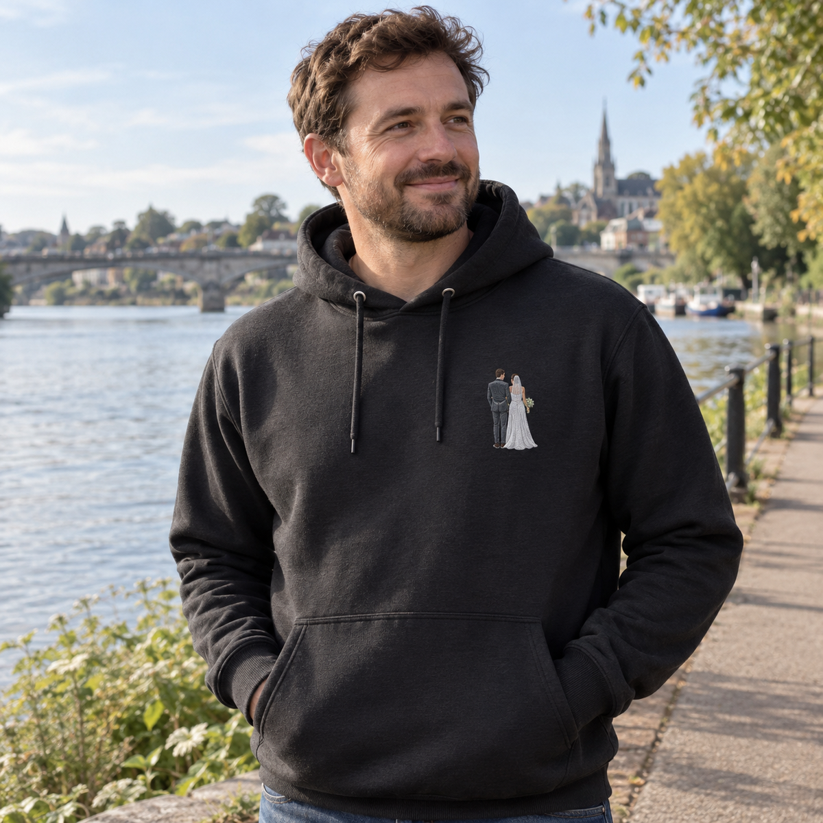 Man wearing a black personalised embroidered photo hoodie with a small full-colour bride and groom wedding portrait by the riverside