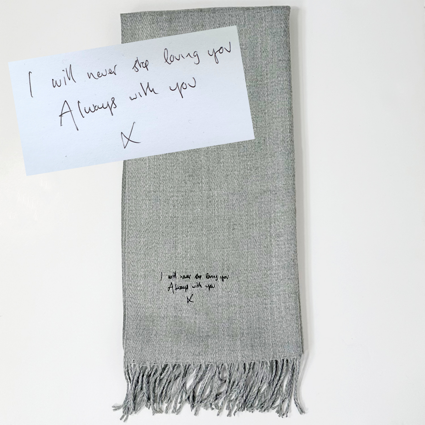 An elegantly embroidered grey scarf with a handwritten message in black thread, personalized just for you. Our luxurious scarf is a perfect blend of craftsmanship and sentimental value, as we bring your unique message to life through exquisite embroidery. Wrap yourself in warmth and cherished memories with this one-of-a-kind scarf