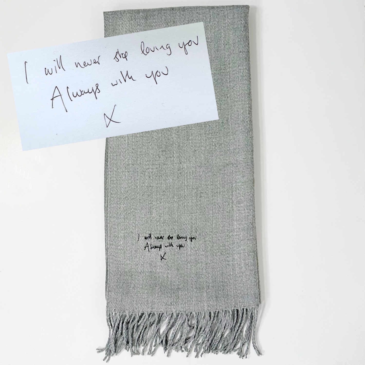 An elegantly embroidered grey scarf with a handwritten message in black thread, personalized just for you. Our luxurious scarf is a perfect blend of craftsmanship and sentimental value, as we bring your unique message to life through exquisite embroidery. Wrap yourself in warmth and cherished memories with this one-of-a-kind scarf